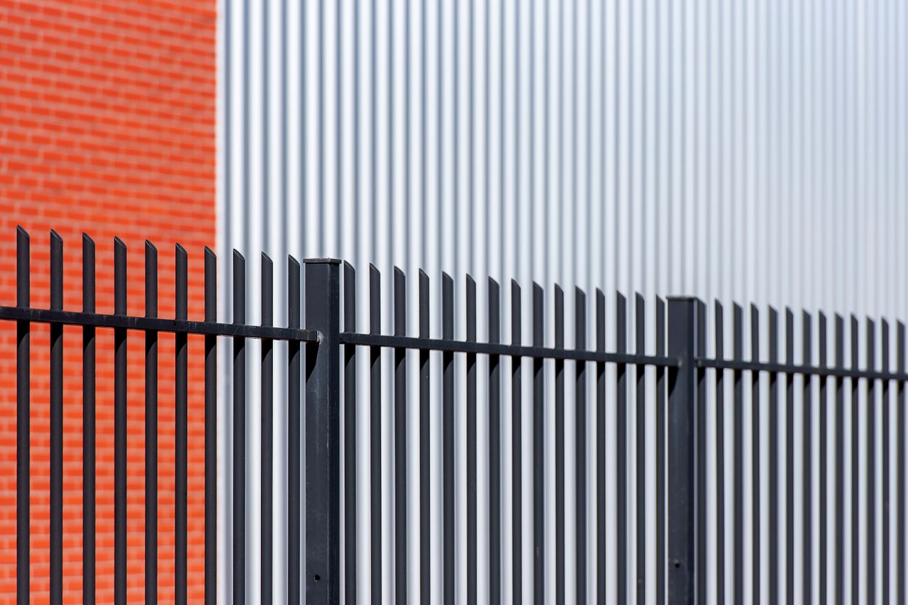 Black metal fence contrasts with red brick and corrugated metal backdrop, offering a sleek industrial look.